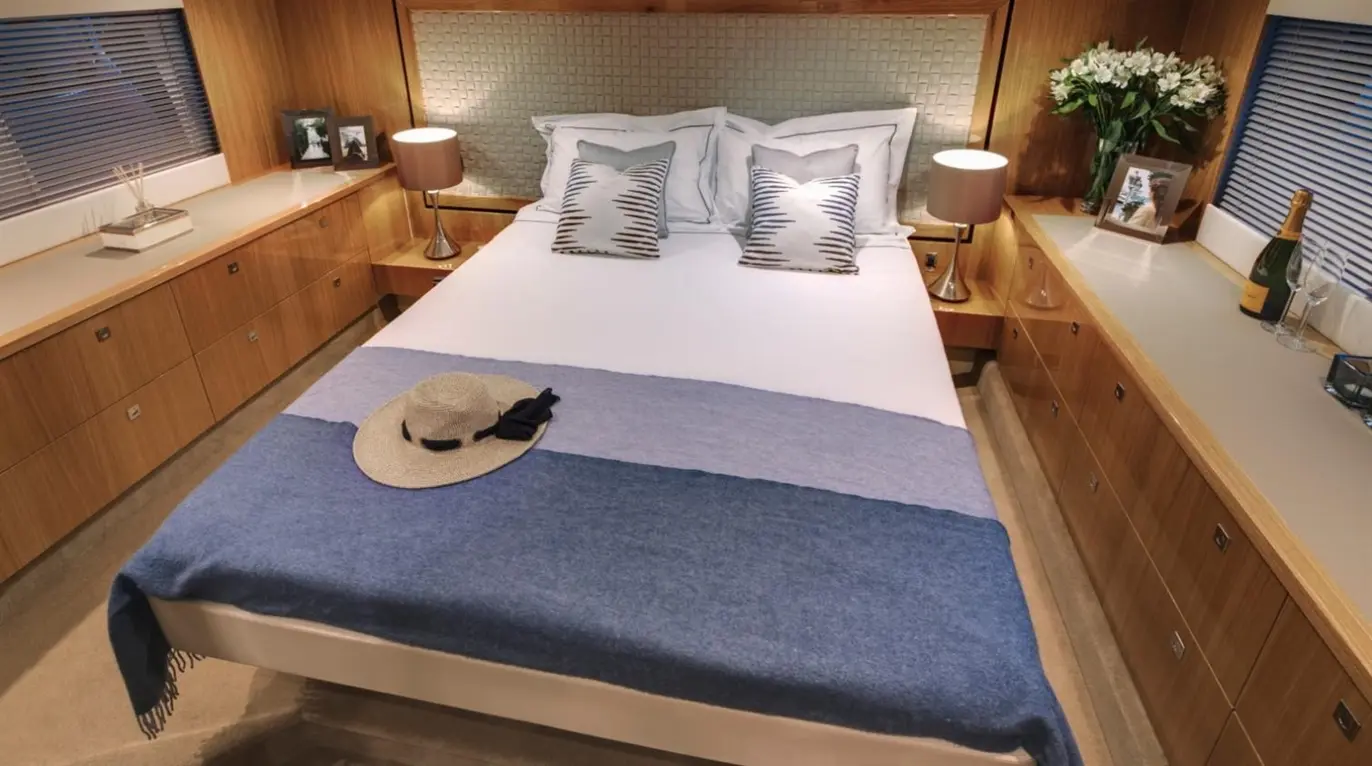 Stylish bedroom with a double bed, blue throw, hat, bedside lamps, floral decor, and champagne on a wooden chest of drawers.